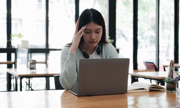 Serious focused Asian student using laptop in kitchen, looking at screen with attention and concentration, watching learning webinar, virtual training, video course, studying from home