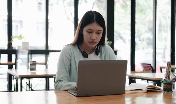 Serious focused Asian student using laptop in kitchen, looking at screen with attention and concentration, watching learning webinar, virtual training, video course, studying from home