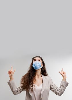 Attractive girl in medical mask points up. Quarantine covid-19 period. Woman weared white formal dress isolated white background. Coronavirus concept