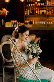 Bride in wedding dress and bridal veil seats on fashion chair in cafe. Advert for social networks for wedding agency and bridal salon.