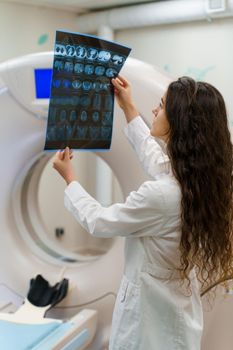 Vertical picture of medical student who looks at x-ray picture of patient brain near kt komputer tomograhphy. Young girl in medical clinic