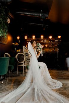 Bride in wedding dress and bridal veil seats on fashion chair in cafe. Advert for social networks for wedding agency and bridal salon.