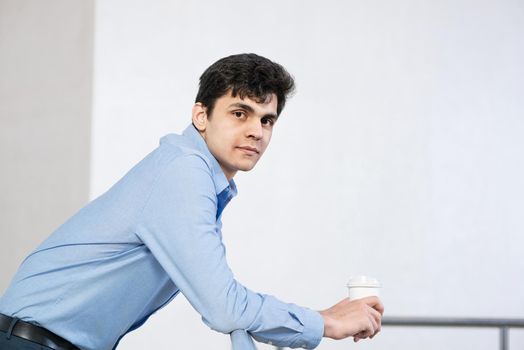 close-up portrait of a successful businessman. holds a paper cup of coffee and rests on a metal railing