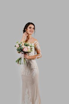 Bride with wedding bouquet smiles, looks right side and touches her face. Attractive girl vertical portrait for social networks. Girl in wedding gown on blank background