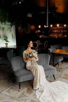 Bride in wedding dress and bridal veil seats on fashion chair in cafe. Advert for social networks for wedding agency and bridal salon.