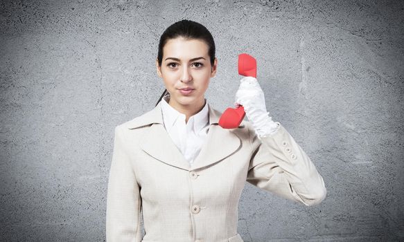 Beautiful business woman with vintage red phone. Elegant call center operator in white business suit posing with landline phone in hand. Business assistance and consultation. Hotline telemarketing