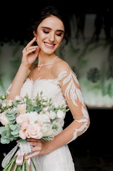 Bride with wedding bouquet smiles and touches her face and hair. Girl in wedding dress in fashion restaurant