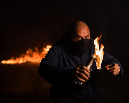 A masked man is holding a burning bottle. Molotov cocktail