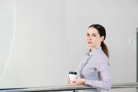 young attractive woman with a paper cup of coffee, rests on railing