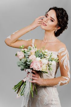 Attractive girl bride with wedding bouquet smiles, looks left side and touches her face. Attractive girl vertical portrait for social networks