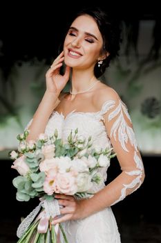 Bride with wedding bouquet smiles and touches her face and hair. Girl in wedding dress in fashion restaurant