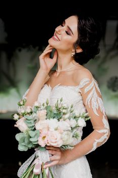 Bride with wedding bouquet smiles and touches her face and hair. Girl in wedding dress in fashion restaurant