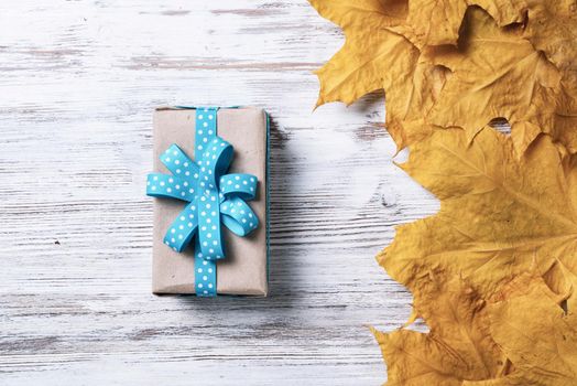 Flat lay autumn composition with gift box and yellow autumn leaves. Holiday present decorated blue ribbon bow on vintage wooden desk. Happy thanksgiving congratulation. Autumn sale advertising.