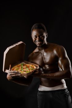 Athletic handsome black man works in pizza delivery. Stay at home and eat a pizza. Tasty food. African man smiles and shows a pizza in cardboard box.
