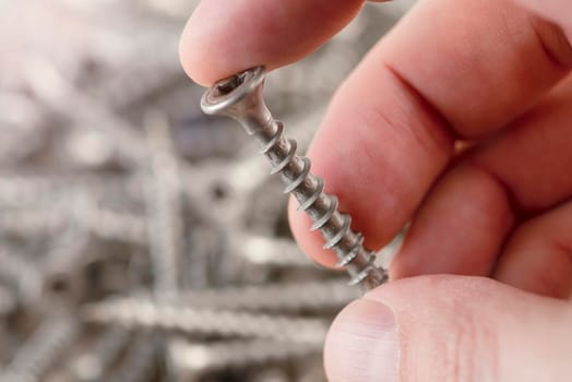 A man holds a screw, close-up. Screws for the production of wooden furniture. Repair and repair tools. Stainless steel bolts