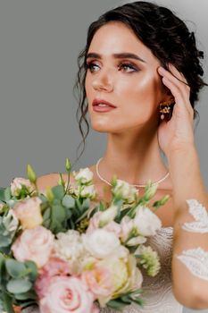 Bride with wedding bouquet smiles and touches her face and hair. Attractive girl portrait for social networks. Girl in wedding gown on blank background