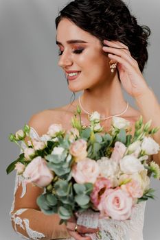 Bride with wedding bouquet smiles and touches her face and hair. Attractive girl portrait for social networks. Girl in wedding gown on blank background