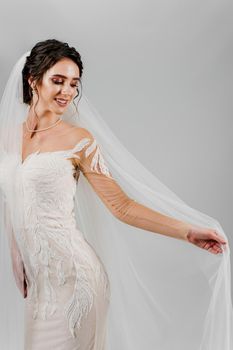 Young attractive bride in wedding dress touches bridal veil on white background in studio. Advert for social networks for wedding agency and bridal salon.