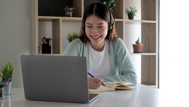 Happy young woman in headphones speaking looking at laptop making notes, girl student talking by video conference call, female teacher trainer tutoring by webcam, online training, e-coaching concept.