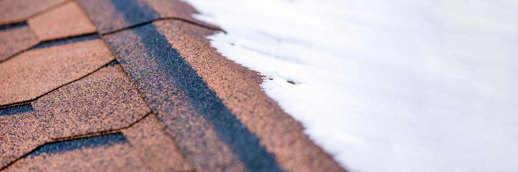 Red shingles. The roof of a house made of shingles is covered with snow in winter, close-up. Frost resistance and elasticity of bituminous tiles in severe frosts