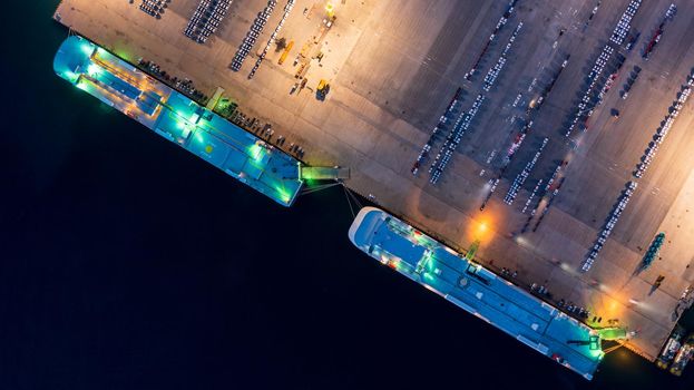New car lined up in the port for import export around the world, Automobile and automotive roro carrier boat vessel terminal, Aerial view rows of new car at night waiting to be dispatch and shipped.