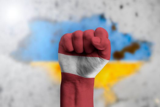 Latvia helps Ukraine and stands in solidarity with it. The concept of humanitarian aid to Ukraine. The fist is painted in the colors of the flag of Latvia against the background of the Ukrainian flag