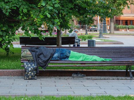 MOSCOW, RUSSIA - June 04, 2018. Homeless man sleeps on street bench. Houseless man covers himself with his clothes and towel.