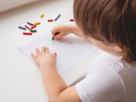 Toddler draws colorful robot. Kid uses wax crayons to paint it. Coloring pages to train fine motor skills.