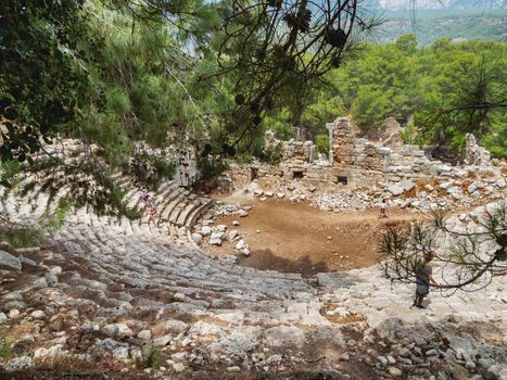 PHASELIS, TURKEY - May 19, 2018. Tourists walk into ruins of amphitheatre of ancient Phaselis city. Panorama view on famous architectural landmark, Kemer district, Antalya province.