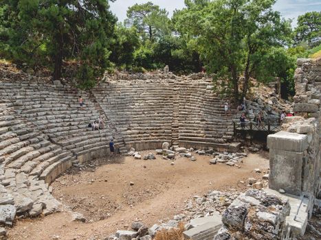 PHASELIS, TURKEY - May 19, 2018. Tourists walk into ruins of amphitheatre of ancient Phaselis city. Panorama view on famous architectural landmark, Kemer district, Antalya province.