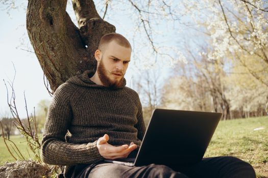 Young man using and typing laptop computer in summer grass.