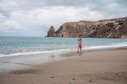 A plump woman in a bathing suit enters the water during the surf. Alone on the beach, Gray sky in the clouds, swimming in winter