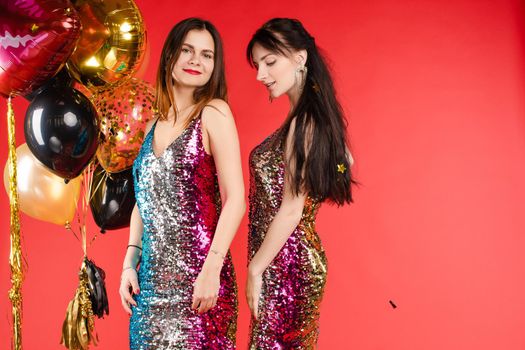 Group smiling beautiful woman posing surrounded by colorful shimmering confetti isolated red studio background. Happy three girl friend enjoying holiday party relaxing and having fun medium long shot