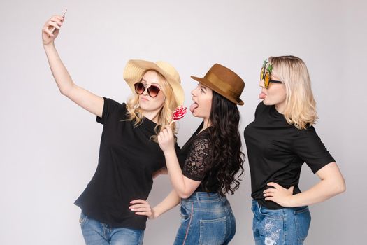 Smiling female friend wearing funny mask hat and eyeglasses posing taking selfie using smartphone medium shot. Happy woman having fun enjoying holiday party isolated at white studio background