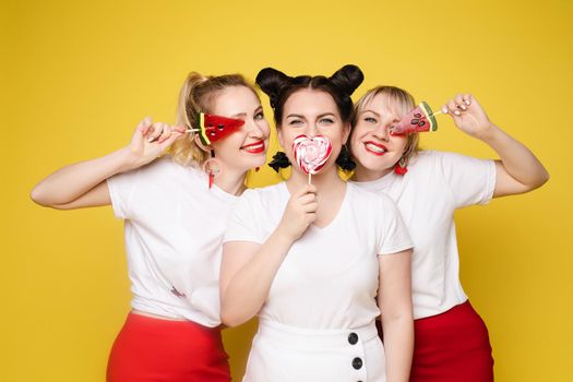 Group beautiful girl friend relaxing together posing with sweet colorful candy at yellow studio background. Happy smiling attractive woman having fun feeling rejoicing and happiness medium long shot