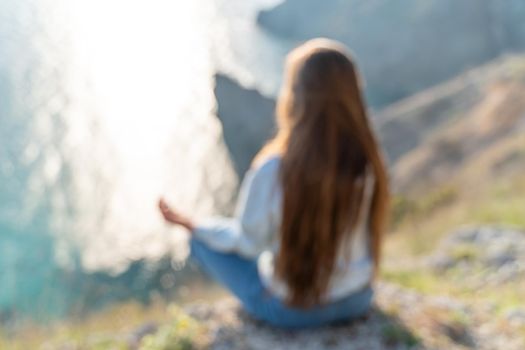 Woman tourist enjoying the sunset over the sea mountain landscape. Sits outdoors on a rock above the sea. She is wearing jeans and a blue hoodie. Healthy lifestyle, harmony and meditation.