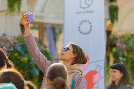 At a city festival, a girl photographs the stage with her mobile phone above her head from a height.Russia Zelenograd April 23, 2022.