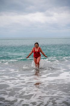 Woman in a bathing suit at the sea. A fat young woman in a red swimsuit enters the water during the surf.