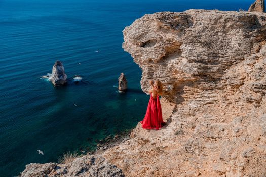 A woman in a red flying dress fluttering in the wind, against the backdrop of the sea