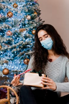 Girl in a medical mask with a Christmas present and candy. celebration of the new year on self-isolation. Pandemic coronavirus covid-19 concept. Advertising sale during the quarantine period