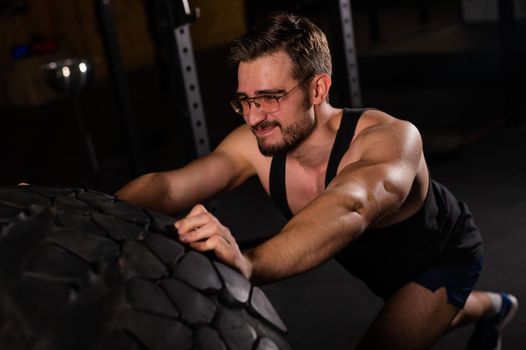 Caucasian man pushing a car tire in the gym