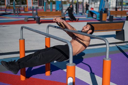 Shirtless man doing horizontal balance on parallel bars at sports ground