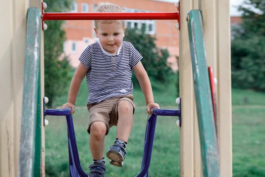 A small boy climbs up to playhouse at public playground in summer time