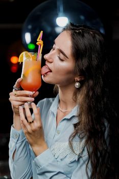 Girl with cocktail is drinking in night club before party. Advert for bar and night clubs. Citrus alcohol drink with orange juice