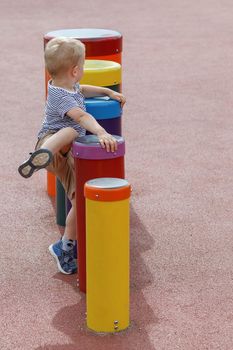 Small boy trying to climb up on a drum in outdoor playground. Lifted leg, climbing up on a line of drums 