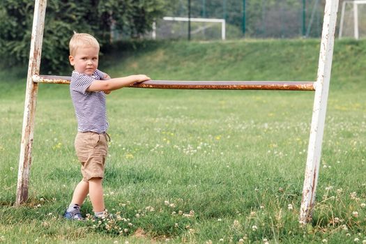 Cute kid posing and looking at camera. Holding old iron railing in a greenfield background.