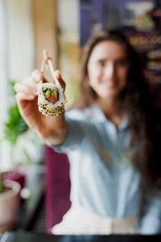Happy girl is giving sushi to you in japanese restaurant. Young girl is holding sushi by chopsticks one piece of roll. Advert for sushi delivery.