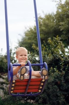 Happy, smiling child is swinging on a swings in a park at summer
