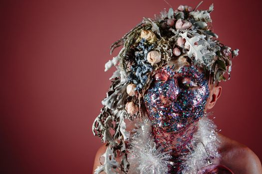 The face of a male model in a headdress of fresh flowers filled with wax.