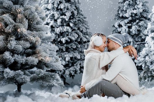 Couple seat on the snow and hug, kiss, and have fun each other. Winter love story before new year celebration. Waiting for christmas gift. Happy couple weared fur headphones, hats, white sweaters.